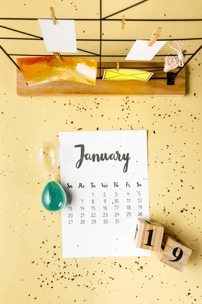 Vista superior del calendario de enero con confeti dorado y tarjetas con pinzas de ropa en beige - foto de stock