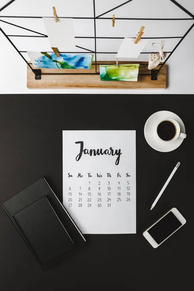 Ansicht des Januarkalenders mit Notizbüchern, Smartphone und Tasse Kaffee am Arbeitsplatz — Stockfoto