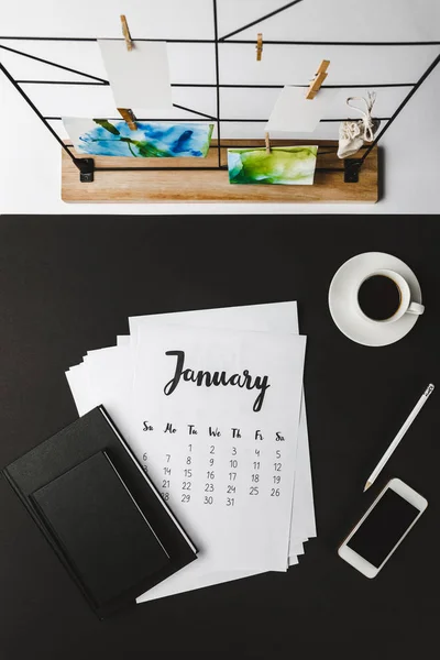 Vista dall'alto del calendario gennaio con quaderni, smartphone e tazza di caffè sul posto di lavoro — Foto stock