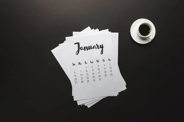 Draufsicht auf Januarkalender und Tasse Kaffee auf schwarz — Stockfoto