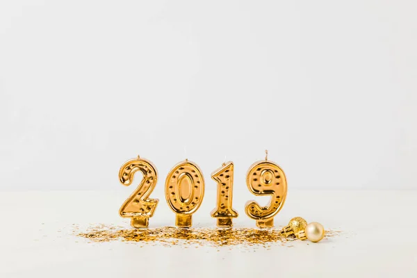 Golden 2019 candles, shiny christmas baubles and confetti on white background — Stock Photo