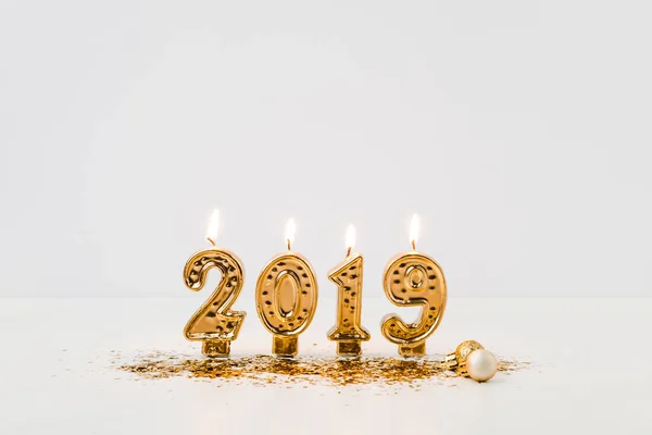 Vue rapprochée des bougies 2019 allumées et des confettis dorés sur fond blanc — Photo de stock