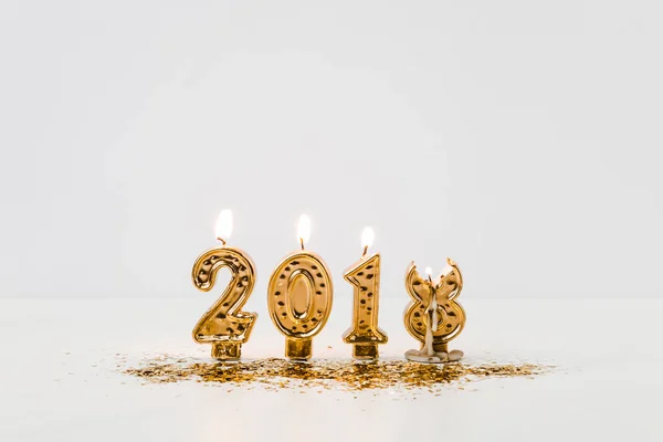 Burning 2018 candles and golden confetti on white background — Stock Photo