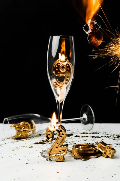 Vista da vicino di bicchieri di champagne con candela, scintillante e numeri dorati 2019 su nero — Foto stock