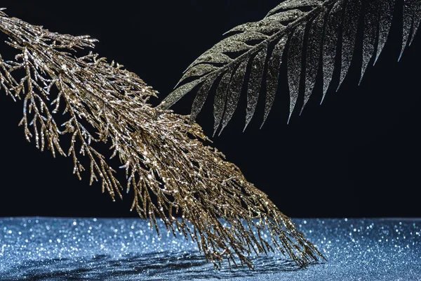 Festive branches decorated by golden glitter over sparkling surface on black — Stock Photo