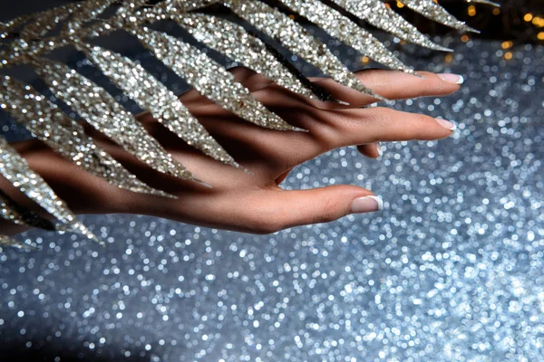 Частичный вид женской руки и украшенная праздничная ветвь над сверкающей поверхностью — стоковое фото