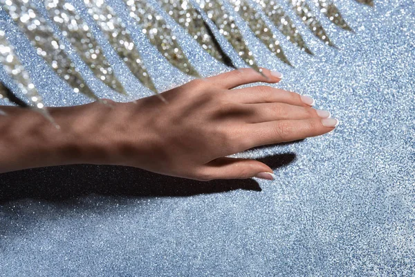 Abgeschnittenes Bild weiblicher Hand und geschmückter festlicher Ast über glitzernder Oberfläche — Stockfoto