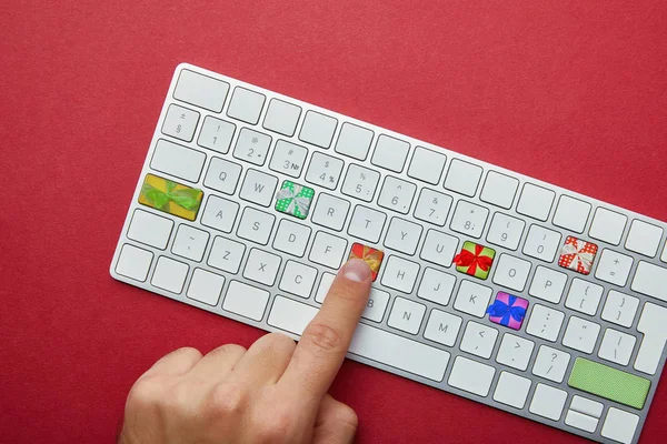 Обрізаний вигляд людини, що штовхає кнопки з подарунками на клавіатурі комп'ютера на червоному тлі, онлайн концепція різдвяних покупок — стокове фото