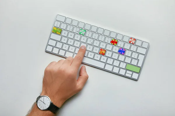 Vista recortada del hombre pulsando el botón en el teclado de la computadora con regalos sobre fondo blanco, concepto de compras de Navidad en línea - foto de stock