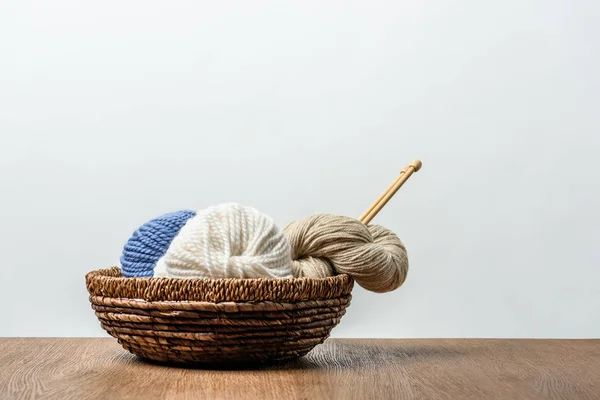 Vista de perto de fios com agulhas de tricô em cesta de vime em mesa de madeira em fundo cinza — Fotografia de Stock