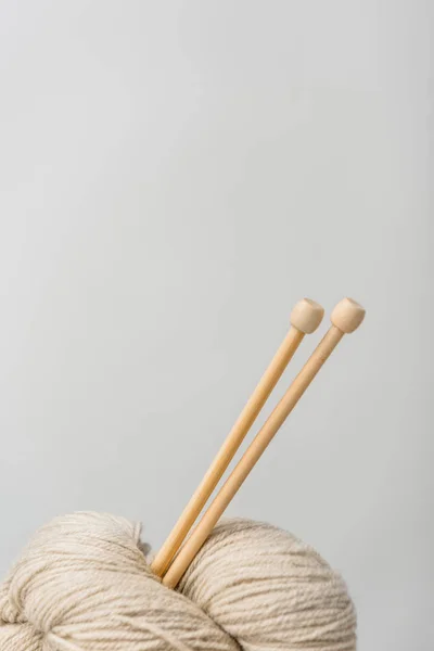 Close up view of beige knitting clews with knitting needles on grey backdrop — Stock Photo