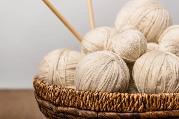 Close up view of yarn clews and knitting needles in wicker basket on grey background — Stock Photo