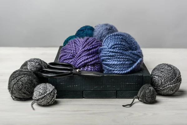 Close up view of yarn balls and scissors in wooden box on white tabletop — Stock Photo