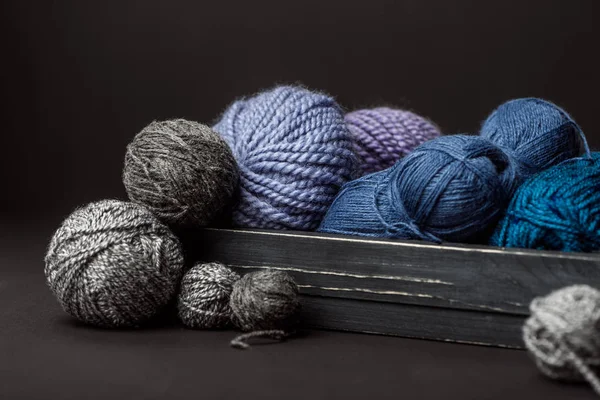 Close up view of grey, purple and blue knitting clews in wooden box on black background — Stock Photo