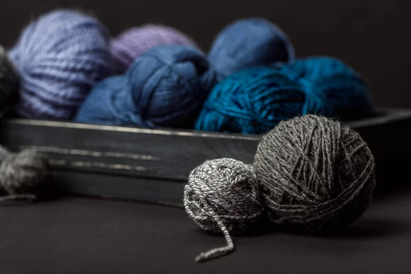 Close up view of grey, purple and blue knitting clews in wooden box on black background — Stock Photo