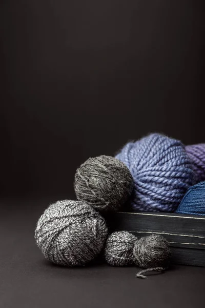 Close up view of grey, purple and blue knitting clews in wooden box on black background — Stock Photo