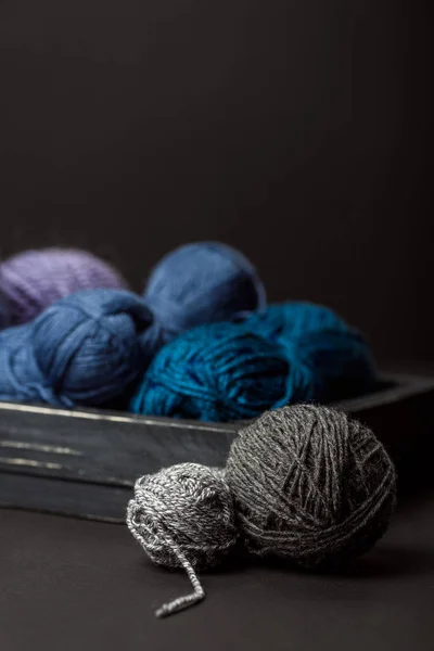 Close up view of grey, purple and blue knitting clews in wooden box on black background — Stock Photo