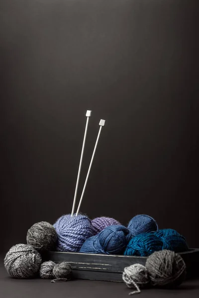 Close up view of knitting clews and knitting needles in wooden box on black backdrop — Stock Photo