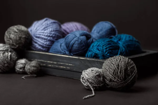 Close up view of grey, purple and blue knitting clews in wooden box on black background — Stock Photo