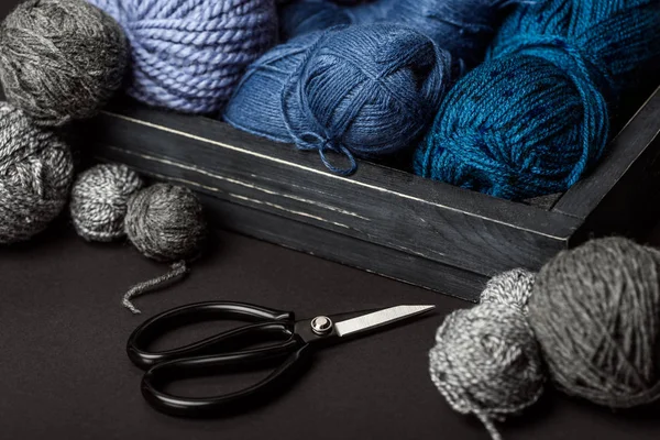 Close up view of grey, purple and blue knitting clews in wooden box on grey tabletop with scissors — Stock Photo