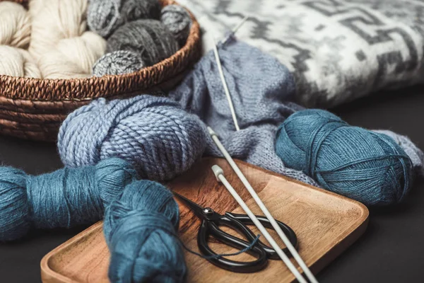 Close up view of knitting, scissors and knitting needles on dark tabletop with blanket — Stock Photo