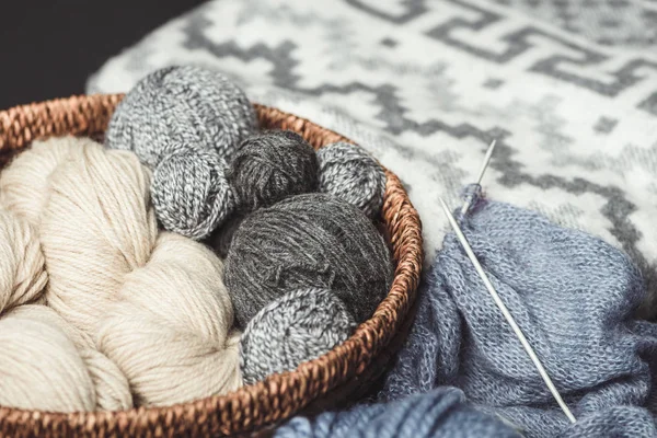 Close up view of knitting clews in wicker basket with grey blanket on background — Stock Photo