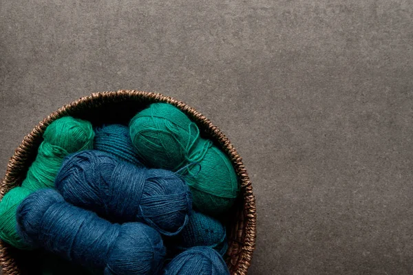 Top view of green and blue yarn clews in wicker basket on grey background — Stock Photo