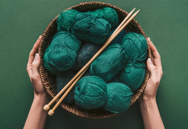 Cropped shot of woman holding wicker basket with yarn and knitting needles on green background — Stock Photo