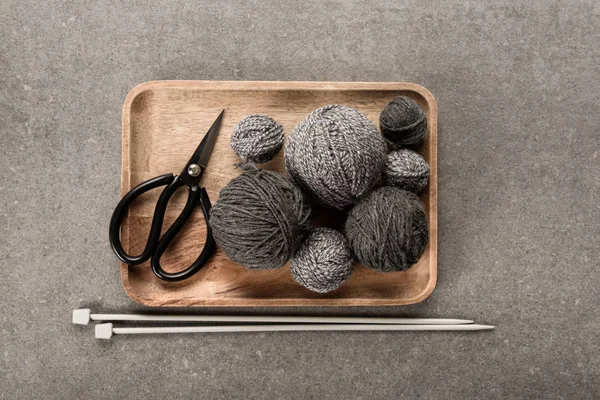 Vue de dessus du tricot gris, ciseaux et aiguilles à tricoter sur fond gris — Photo de stock