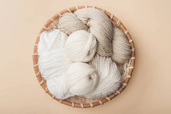 Top view of white and beige yarn in wicker basket on beige background — Stock Photo