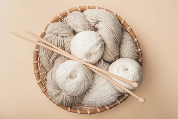 Top view of yarn and knitting needles in wicker basket on beige background — Stock Photo