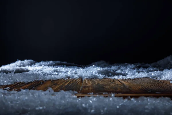 Braunes Holzbrett mit Schnee bedeckt auf schwarz — Stockfoto