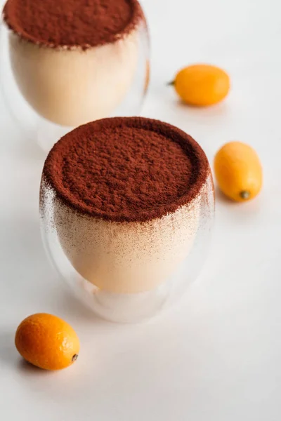 Vasos con postres de tiramisú y cacao en polvo sobre mesa con kumquats - foto de stock