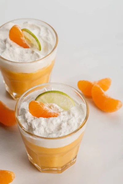 Dos vasos con dulces postres cítricos con rebanadas de mandarina y lima - foto de stock