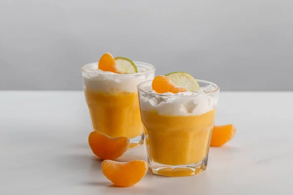 Dos vasos con postres de crema con mandarina y rodajas de lima - foto de stock