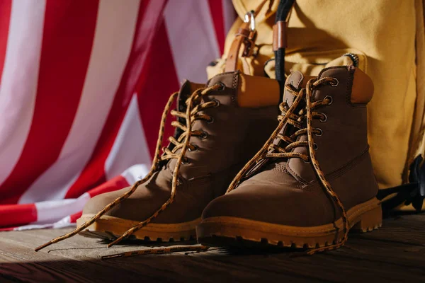 Close-up view of trekking boots, backpack and american flag on wooden surface, travel concept — Stock Photo
