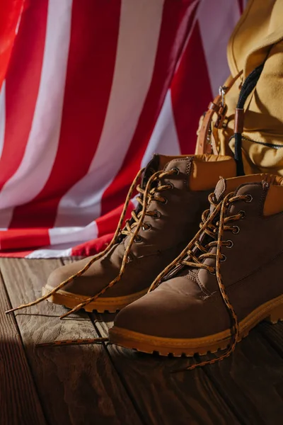 Vista ravvicinata di scarponi da trekking, zaino e bandiera americana su superficie in legno — Foto stock