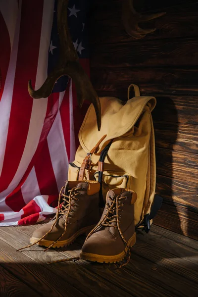 Bottes de trekking, sac à dos, cornes et drapeau américain sur la surface en bois — Photo de stock