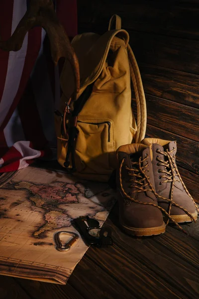 Vista de cerca de botas de trekking, equipo de senderismo, mapa, mochila y bandera americana en superficie de madera - foto de stock