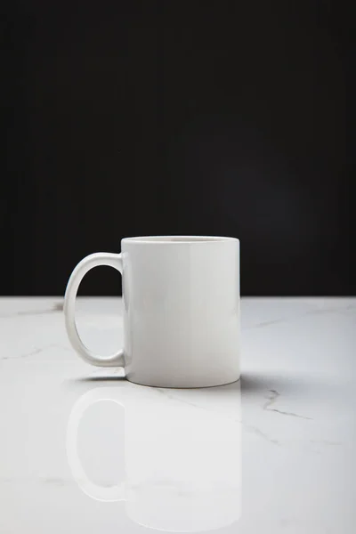 Vue rapprochée de la tasse blanche réfléchie sur la surface blanche sur le noir — Photo de stock