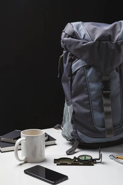 Mochila, smartphone, taza y brújula en negro, concepto de viaje - foto de stock