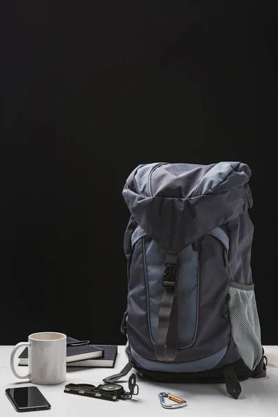 Рюкзак, чашка, ноутбуки, смартфон и туристическое оборудование на черном — стоковое фото