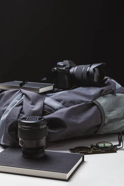 Mochila, câmera fotográfica com lente, cadernos com caneta e bússola em preto — Fotografia de Stock