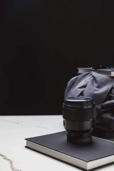 Close-up view of photo lens on notebook and backpack on black — Stock Photo