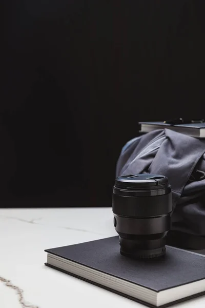 Vue rapprochée de l'objectif photo sur ordinateur portable et du sac à dos sur noir — Photo de stock