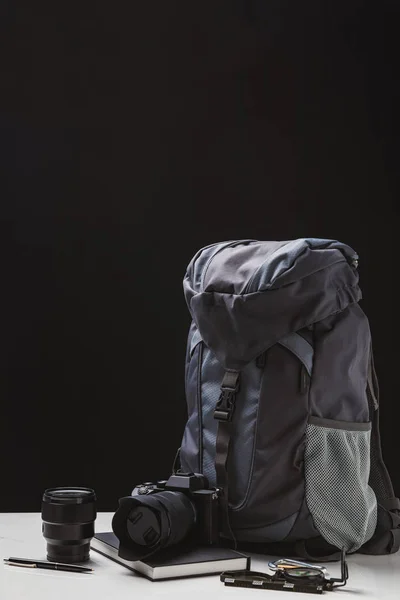 Mochila, câmera fotográfica com lente, notebook e equipamento de trekking em preto — Fotografia de Stock
