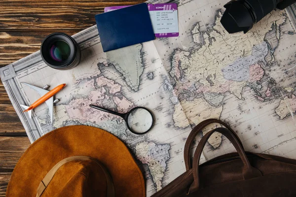 Вид зверху на коричневу шкіряну сумку, капелюх, збільшувальне скло, маленька модель площина, фотоапарат, лінза та паспорт з посадковим талоном на карті — стокове фото