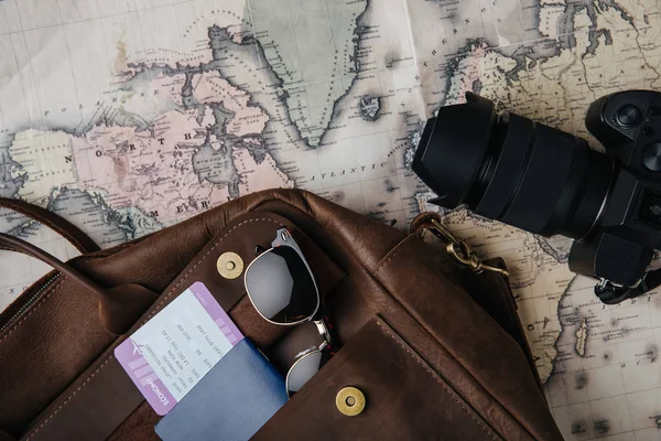 Vista superior de la bolsa de cuero con pasaporte, billete, gafas de sol, cámara y mapa - foto de stock