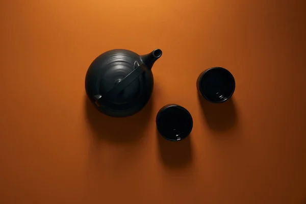 Вид зверху на чорний керамічний чайник з чашками на коричневому фоні — стокове фото