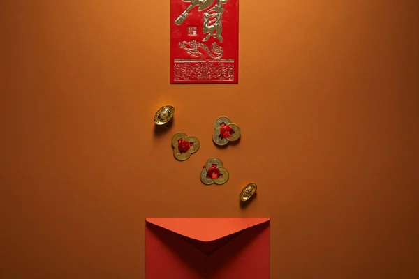 Vista superior de sobre rojo, decoraciones chinas doradas y jeroglífico sobre fondo marrón - foto de stock